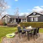 Schwarzes Holzhaus mit Terrasse und Garten. Außentisch mit Stühlen und Sandkasten.
