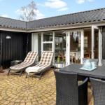 Terrasse mit Liegen, Tisch und Stühlen. Durchgehende Glasfront zum Innenraum.