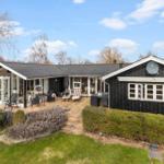 Schwarzes Holzhaus mit Terrasse und Garten. Satellitenschüssel und Fenster sichtbar.
