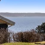 Haus mit Blick auf ruhiges Wasser und bewaldeten Hügeln im Hintergrund.