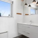 Badezimmer mit Waschbecken, Spiegel und Fenster mit Pflanze.