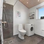 Bad mit Dusche, Toilette und Waschmaschine. Fenster mit Pflanzen und Holzdecke.