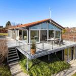 Moderne Villa mit großem Balkon, Glasfront und Terrasse mit Sitzgelegenheit.