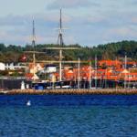 Hafenstadt mit Segelschiff und roten Dächern am Wasser