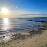 Sonnenlicht spiegelt sich auf dem Wasser. Strand mit Steinen und Wellen.