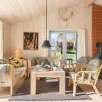 Wohnzimmer mit Holzwänden, Kamin und Sitzgelegenheiten. Fenster zur Außenterrasse.