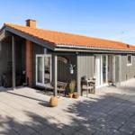 Ein Haus mit Terrasse, Glasfronten und rotem Ziegeldach. Außenbereich mit Möbeln und Pflanzen.