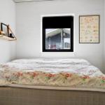 Schlafzimmer mit Bett, Fenster und Wandbild. Regal mit Büchern und Dekoration.