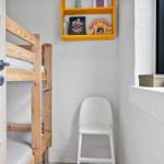 Kinderzimmer mit Holz-Etagenbett, weißer Stuhl und gelbem Regal an der Wand.