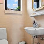 Badezimmer mit Toilette, Waschbecken und Fenster mit Pflanzen.