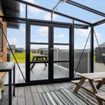Terrasse mit Glasdach, Holztisch und Sitzmatte. Blick auf Garten und Nachbarhäuser.