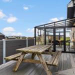 Terrasse mit Holzpicknicktisch und Glasüberdachung neben Backsteinhaus.