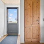 Eingangsbereich mit Holztür, Fenster und Kaminofen. Boden aus Holz, Wandfarbe Weiß.