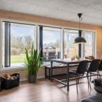 Wohn- und Essbereich mit Holzwand, Kamin und großem Fensterblick auf Garten.