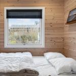 Schlafzimmer mit Holzwänden, Bett und Fenster mit Blick nach draußen.