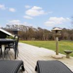 Terrasse mit Tisch, Stühlen und Liegestühlen. Grünfläche mit Spielgeräten und Steinobjekten.