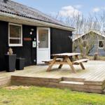 Holzterrasse mit Picknicktisch vor schwarzem Ferienhaus mit weißen Fenstern und Tür.