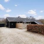 Schwarzes Ferienhaus mit Holzterrasse und Kiesfläche. Hinterhof mit Hecke und Tor.