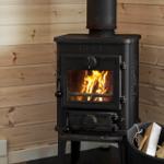 Holzofen mit brennendem Feuer in einem Raum mit Holzwandverkleidung und Holzstapel daneben.