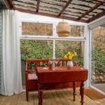 Roter Tisch mit Stuhl und Blumen vor Fenster mit Blick auf Garten.