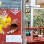 Roter Tisch mit Weinflaschen, Würfeln und Blumen vor Fenster.