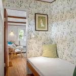 Schlafzimmer mit floraler Tapete und Bett. Durchgang in Wohnzimmer mit Sofa und Stuhl.
