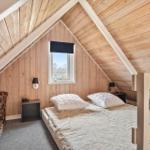 Schlafzimmer mit Doppelbett, Fenster und Holzwandverkleidung.