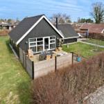 Schwarzes Haus mit Terrasse und Garten. Holzgeländer und Pflanzen sind sichtbar.