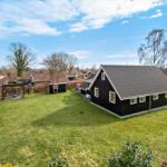 Schwarzes Haus mit großem Garten und Terrasse unter blauem Himmel.