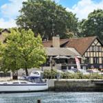 Haus mit Bootshafen und Parkplatz. Holzhaus mit Terrasse und Wasser.