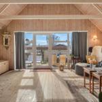 Wohnzimmer mit Holzdecke, Glasfront und Sofa mit Kissen.