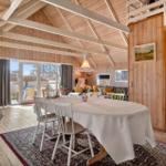 Ein Esszimmer mit Holzwand und -boden, großem Tisch und Sicht auf die Terrasse.