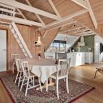 Essbereich mit Tisch und Stühlen unter Holzdecke. Küche und Wohnbereich im Hintergrund.