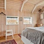 Schlafzimmer mit Holzwand, Bett, Fenstern und Stufenstuhl.