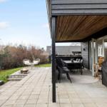 Terrasse mit Sitzgruppe, Esstisch und Grill. Außendiele mit Feuerkorb und Pflanzen.