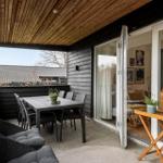 Terrasse mit Tisch, Stühlen und Pflanzen. Durchgehende Glastüren führen ins Innere.
