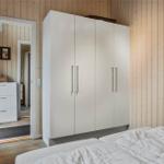 Schlafzimmer mit weißem Schrank und Holzwand. Tür führt in angrenzenden Raum.