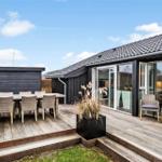 Terrasse mit Sitzgruppe, Tisch und Pflanze vor einem Haus mit Glasfront.