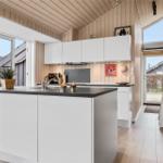 Küche mit weißen Schränken, Holzdecke und Fenstern. Eine Leiter lehnt an der Wand.