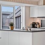 Küche mit weißer Einbauküche, dunklem Arbeitsplatz und Glasfront zur Terrasse.