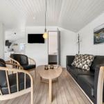 Wohnzimmer mit Sofa, zwei Sesseln und Holztisch. Hintergrund zeigt Küche und Schlafzimmer.