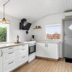 Küche mit weißen Schränken, Holzboden und Fenstern. Küchenzeile mit Herd und Kühlschrank.