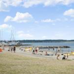 Strand mit Booten, Leuten und Rettungswache unter blauem Himmel.