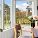 Esstisch mit Stühlen vor großem Fenster mit Blick auf Garten.