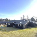 Black wooden house with skylights and solar panels on a green plot.