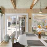 Dining area with round table, white chairs, and view to garden. Wooden ceiling and white furniture.