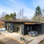 Modern villa with wooden terrace, seating, and view of forest.