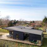 Modern villa with wooden terrace and garden. Greenery and trees surround the house.