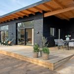 Modern wooden cabin with terrace, garden furniture, and view of the beach.