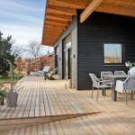 Wooden terrace with dining set and sun loungers in front of modern house.